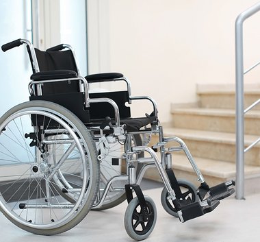 ein Rollstuhl steht vor einer Treppe, die ohne Hilfe nicht zu überwinden ist 
