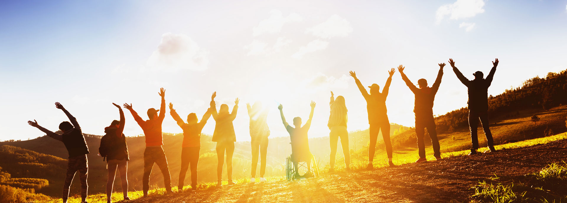 Personen mit Rollifahrer in der Mitte jubeln zur Sonne